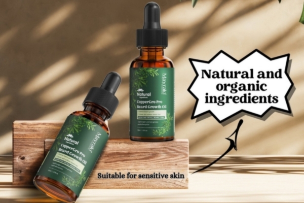 Two bottles of CopperGro Pro Beard Growth Oil with green labels rest on wooden blocks under soft natural lighting, highlighted by text that reads "Natural and organic ingredients" and "Suitable for sensitive skin."