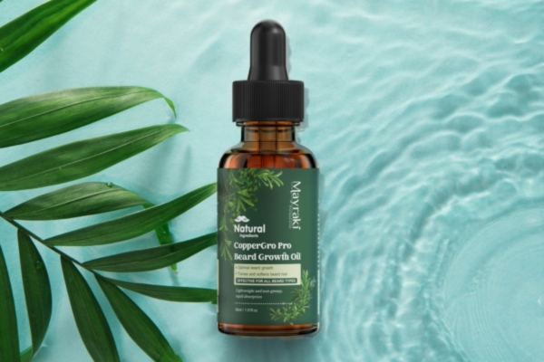 A bottle of Mayzak Natural CopperGro Pro Beard Growth Oil is placed against a serene aqua background with rippling water and green leaves. The natural elements emphasize the product’s organic ingredients and soothing qualities.