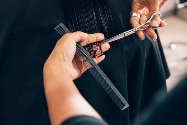 A close-up of a hairdresser trimming the ends of straight, wet hair using scissors and a black comb. The precise cut and professional technique highlight hair maintenance and the importance of regular trims for healthy hair.