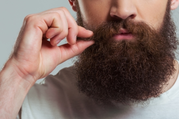 Close-up of a man with a thick, full beard gently tugging on his mustache, showing a well-hydrated and groomed look that can be achieved using Mayraki’s beard oil for hydration.