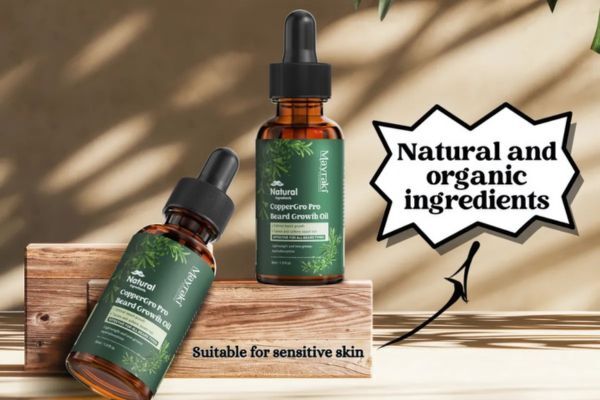 Two amber dropper bottles of Mayraki Natural CopperGro Pro Beard Growth Oil are displayed on a wooden stand with bold text stating “Natural and organic ingredients” and “Suitable for sensitive skin.” The setup highlights the product's gentle formulation and eco-conscious branding.