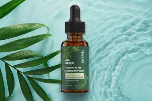 A bottle of “Natural CopperGro Pro Beard Growth Oil” lies flat against a rippling aqua background beside green palm leaves, highlighting a clean and natural aesthetic.