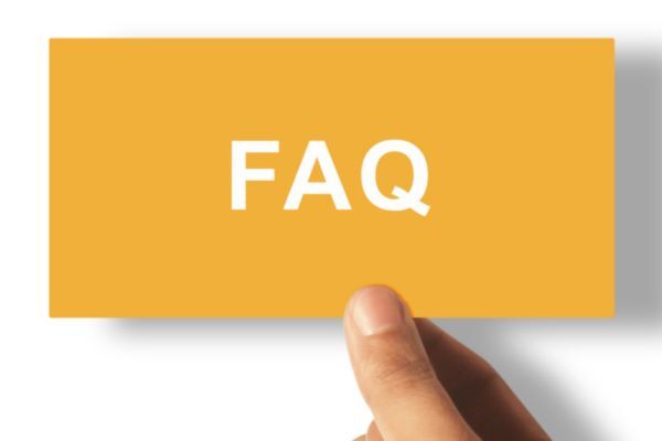 A close-up of a hand holding a rectangular mustard-yellow card with the text “FAQ” printed in bold white letters, symbolizing a frequently asked questions section.