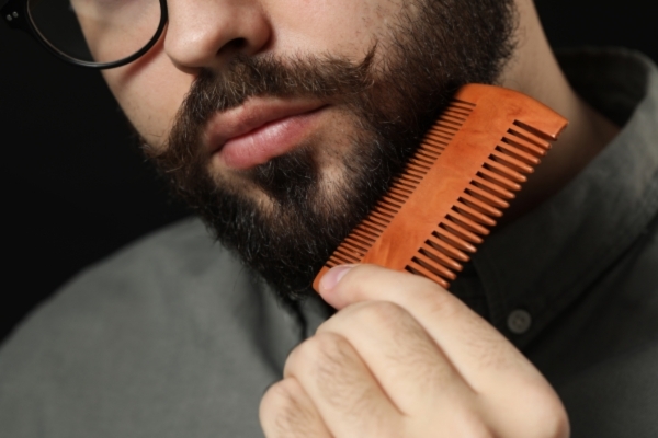 Man combing his beard with a wide-tooth, orange wooden comb, demonstrating the use of a quality tool—an essential factor when choosing the best beard comb for grooming and detangling.