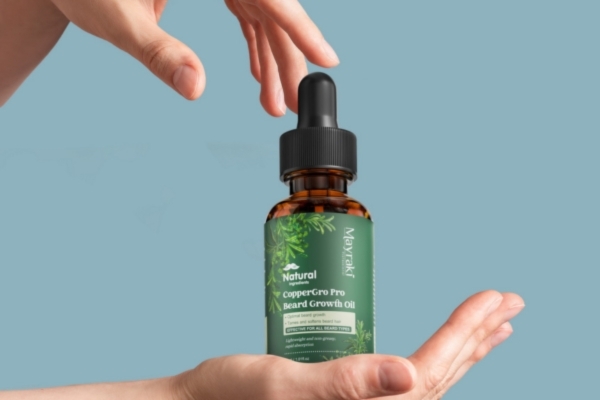 Hands gently framing a bottle of Mayraki CopperGro Pro Beard Growth Oil against a blue background, emphasizing the product's protective qualities for beard care during outdoor activities.