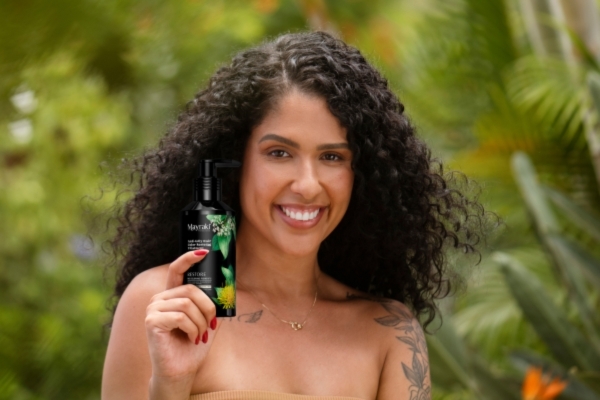 How Your Anti‑Grey Treatment Fits In Smiling woman with healthy, curly hair holding a bottle of Mayraki hair product outdoors, representing natural antioxidant-rich formulas that support strategies to prevent premature graying.