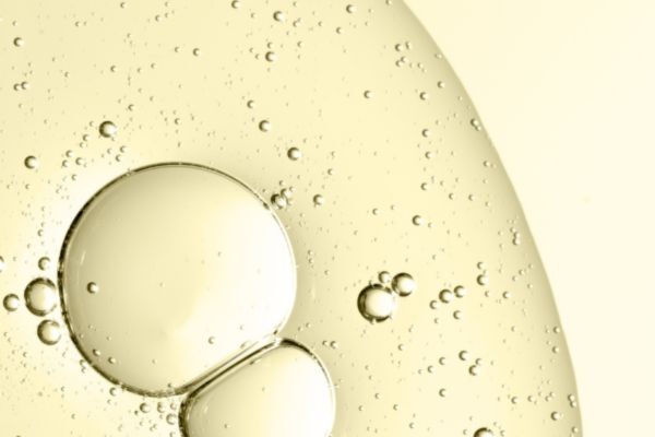 A close-up of translucent golden beard oil droplets suspended in liquid, creating a smooth, abstract texture against a light background.