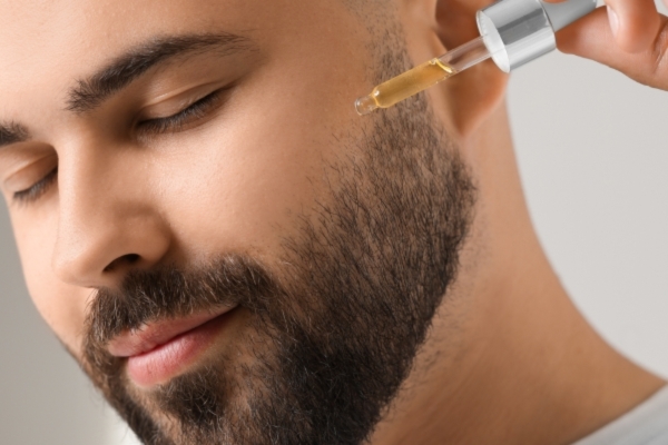 Key Steps in an Effective Nighttime Beard Routine Man applying beard oil with a dropper to his jawline, part of a nighttime beard routine focused on hydration and beard care while the skin rests overnight.