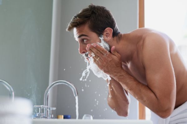A man washing his face at the bathroom sink, illustrating the first step in Mayraki CopperGro Pro Beard Oil usage—cleansing the beard area before applying oil for optimal absorption.