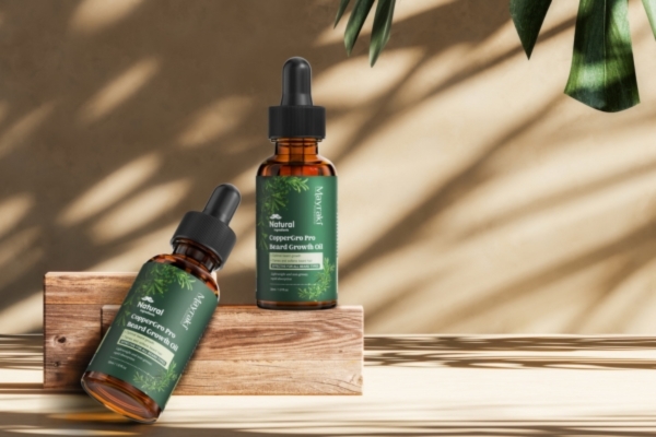 Two amber glass dropper bottles of "Natural CopperGro Pro Beard Growth Oil" displayed on a wooden platform with leafy shadows on a beige background.