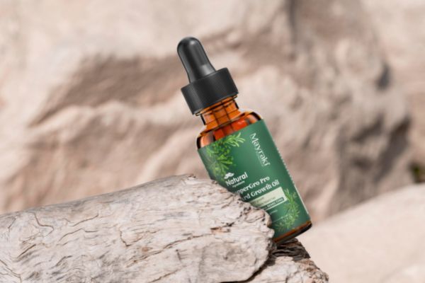 A bottle of Mayraki CopperGro Pro Beard Growth Oil lying diagonally on a piece of driftwood against a rocky natural backdrop, emphasizing its earthy and organic branding.