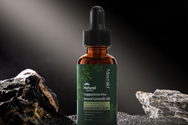  A bottle of Mayraki Natural CopperGro Pro Beard Growth Oil with a dropper cap, placed between rugged black and white stones under a dramatic spotlight. The green label features botanical illustrations and emphasizes its natural, plant-based ingredients.