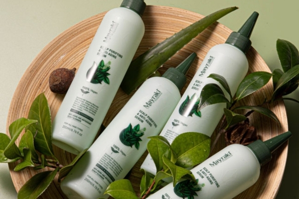 Mayraki Itchy scalp products Four Mayraki Scalp Purifying and Anti-Hair Loss Solutions are arranged in a wooden bowl with aloe vera leaves and green foliage. The natural setup underscores the plant-based formula aimed at nourishing the scalp and promoting healthy hair growth.
