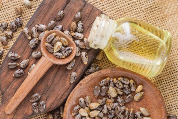 A bottle of castor oil surrounded by scattered castor beans on burlap fabric and wooden boards, highlighting a natural topical remedy commonly used for hair and beard care.