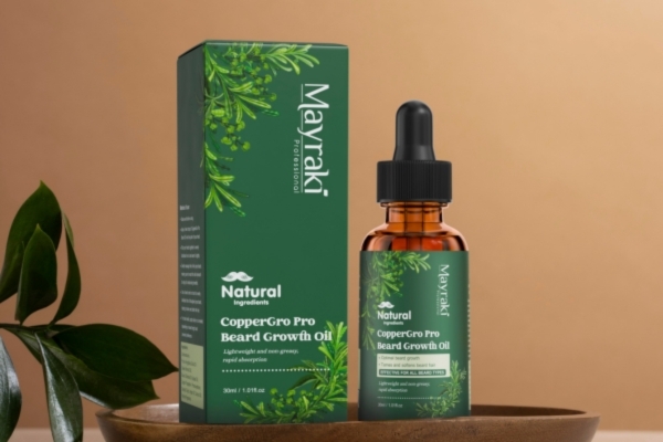 A bottle of Mayraki CopperGro Pro Beard Growth Oil with a dropper top sits next to its matching green box, both decorated with herbal graphics and the text highlighting natural ingredients for beard growth.
