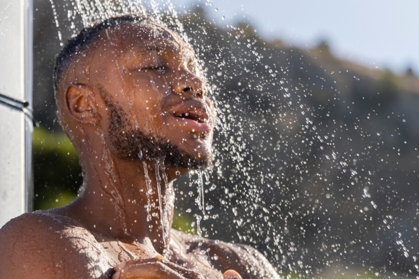 Pre- and Post-Swim Beard Care Routine A man enjoying an outdoor rinse under a shower, water cascading over his beard and face, capturing the refreshing start of a Pre- and Post-Swim Beard Care Routine that helps protect facial hair from chlorine and saltwater damage.