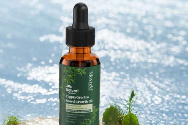 A bottle of Mayraki CopperGro Pro Beard Growth Oil stands in front of a shimmering water background, surrounded by small plants. The label highlights natural ingredients and the product’s purpose to promote beard growth.