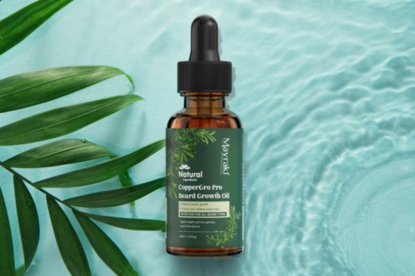 A bottle of Mayraki CopperGro Pro Beard Growth Oil placed on a tranquil aqua background with rippling water and palm leaves, emphasizing its natural ingredients and refreshing, plant-based formulation.