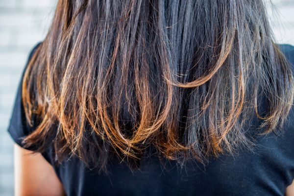 Close-up of the back of a person with shoulder-length dark brown hair showing signs of UV damage, including dryness and lighter, brassy-colored ends