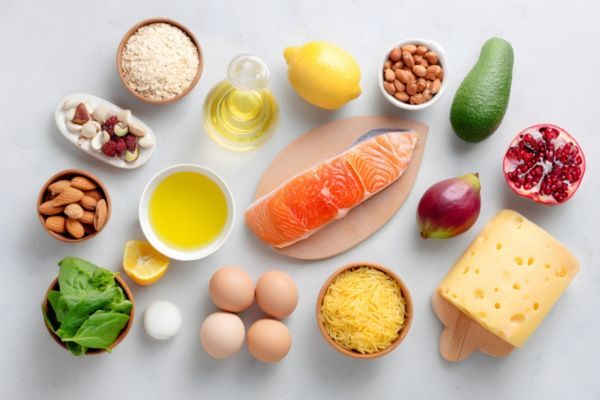 Top Foods That Support Hair Pigment Flat lay of nutrient-rich foods including salmon, eggs, leafy greens, avocado, cheese, nuts, seeds, and oils, all arranged on a white surface. This image supports Hair Mayraki’s philosophy that healthy hair starts with a balanced, vitamin-packed diet.