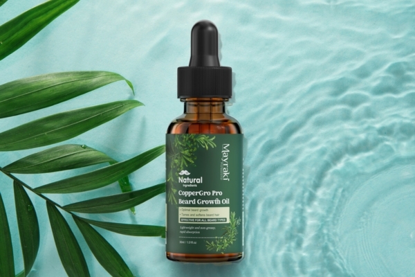 A bottle of Mayraki CopperGro Pro Beard Growth Oil placed on a light aqua background with water ripples and tropical leaves, showcasing its natural, eco-friendly formulation designed to boost beard shine and growth.