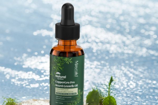 A bottle of Mayraki CopperGro Pro Beard Growth Oil set on a natural surface with small plants, placed in front of a sparkling water background for a fresh, natural vibe.